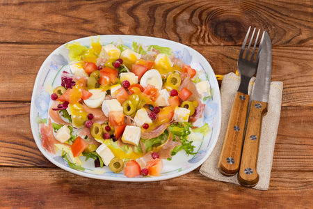 Serving of salad made with jamon slices, boiled quail eggs, soft cheese, fresh different greens and vegetables on a dish on a rustic tableの写真素材