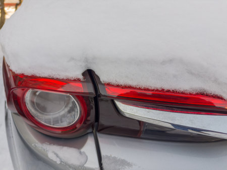 Fragment of rear of parked gray car with tail lamps and brake lights block, covered with fluffy snow above, close-up in overcast weatherの写真素材