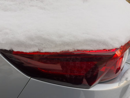 Fragment of rear of parked gray car with tail lamps and brake lights block, covered with fluffy snow above, close-up in overcast weatherの写真素材