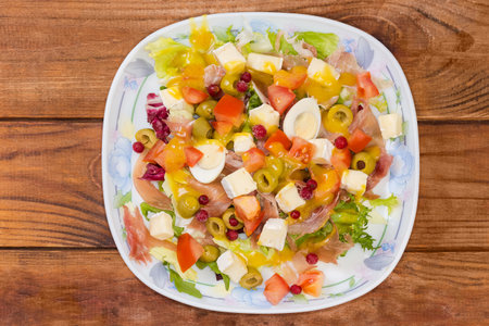 Serving of salad made with jamon slices, boiled quail eggs, soft cheese, fresh different greens and vegetables on a dish on a rustic table, top viewの写真素材
