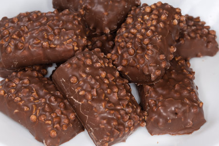 Heap of cookies with puffed rice balls on the tops, covered with milk chocolate on a dish, top view close-up in selective focusの写真素材