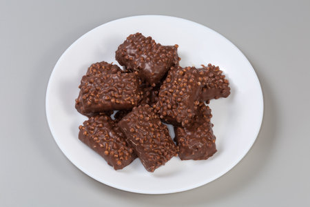 Cookies with puffed rice balls on the tops, covered with milk chocolate on a dish on a gray backgroundの写真素材