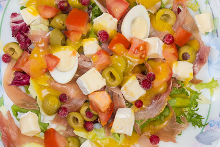Salad made with jamon slices, boiled quail eggs, soft cheese, fresh different greens and vegetables on a dish, top view close-upの写真素材