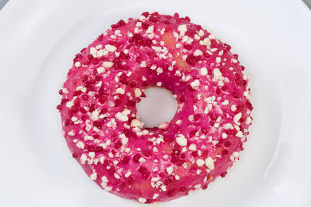 American-style ring shaped donut with raspberry filling, pink glaze and sprinkles on a white dish, top view close-upの写真素材