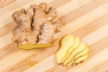 Partly sliced fresh ginger root on a bamboo cutting board, top view close-up