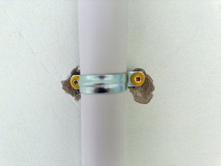 Plastic pipe, as duct for pulling of communication cables fixed to a concrete wall with metal pipe clamp and screws indoor, close-up in selective focusの写真素材