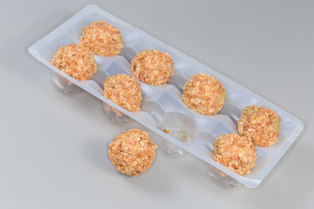 Cookies wafer balls with crushed nut covering and peanut cream filling in the plastic packaging and one ball beside on a gray backgroundsの写真素材