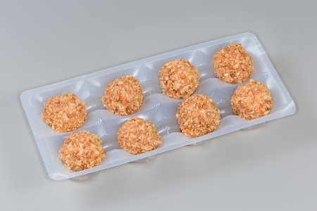 Cookies wafer balls with crushed nut covering and peanut cream filling in the plastic packaging on a gray backgroundsの写真素材