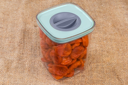 Dried smoked apricots in transparent container with closed lid on a surface covered with a burlapの写真素材