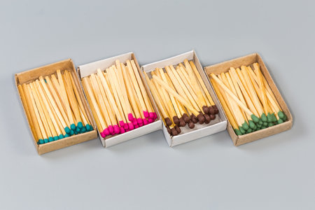 Several open usual cardboard matchboxes with wooden household safety matches with heads of different colors on a gray surfaceの写真素材