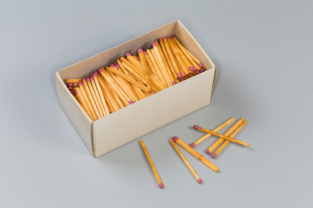 Wooden household safety matches in open large cardboard matchbox and several the same matches beside on a gray surfaceの写真素材
