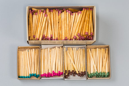 One big and several usual open cardboard matchboxes with wooden household safety matches with heads of different colors on a gray surface, top viewの写真素材