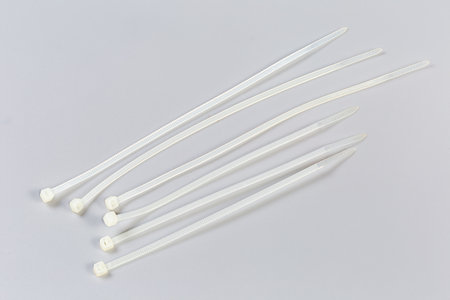 Several unfastened single-use nylon white translucent cable ties of different lengths on a gray backgroundの写真素材