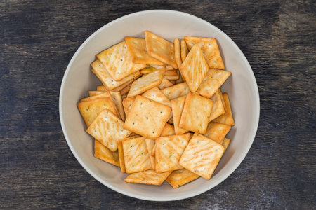 Salty crackers square shape with onion content in bowl on a black surface, top viewの写真素材