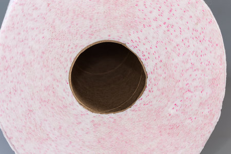 Roll of disposable paper towels with tear-off sheets on a gray surface, view from end, fragment...