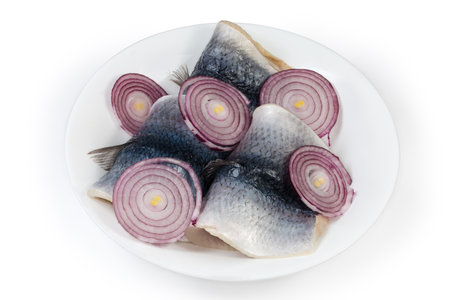 Pickled herring fillets on skin with fresh red onion sliced into rings on the white dish on a white backgroundの写真素材