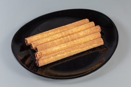Wafer tubes with filling of chocolate cream on a black dish on a gray backgroundの写真素材