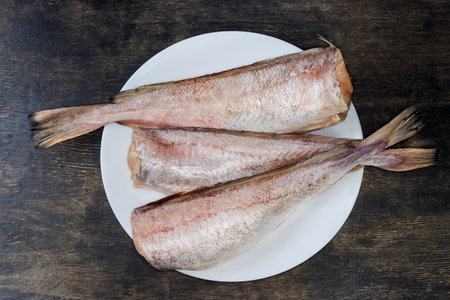 Cooled carcasses of the red cod without heads, cleared from fish scales on white dish on a black...