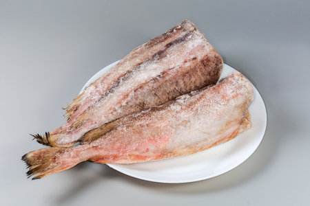Frozen carcasses of the red cod without heads, covered with hoarfrost on white dish on a gray backgroundの写真素材