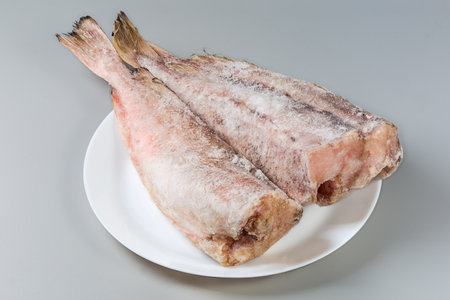 Frozen carcasses of the red cod without heads, covered with hoarfrost on white dish on a gray backgroundの写真素材