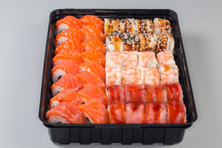 Set of the various sushi in open black plastic packaging for take-out food on a gray background, close-up in selective focusの写真素材