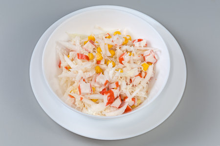Serving of the salad of chopped crab sticks and napa cabbage and sweet corn in the white bowl on a gray backgroundの写真素材