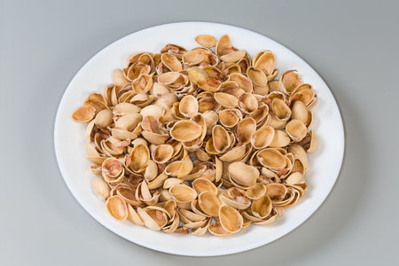 Heap of the empty shells from roasted pistachio nuts after peeling of nut kernels on a dish on a gray backgroundの写真素材