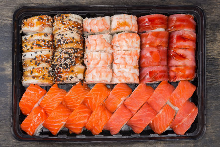Set of the various sushi in open black plastic packaging for take-out food on a black surface, top view close-upの写真素材