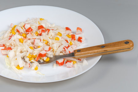 Serving of the salad of chopped crab sticks and napa cabbage and sweet corn on the white dish with fork on a gray backgroundの写真素材