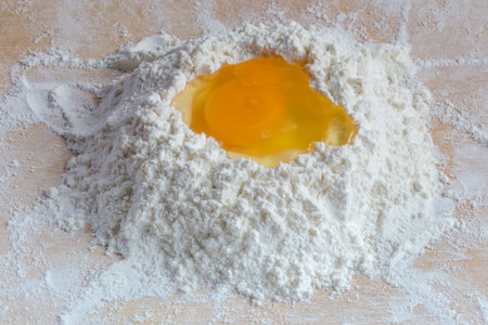 Broken egg in the center of a heap of sifted wheat flour on a wooden board, close-upの写真素材