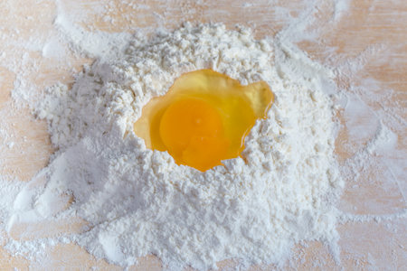 Broken egg in the center of a heap of sifted wheat flour on a wooden board, top view close-upの写真素材