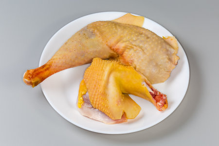 Raw leg and shoulder of rooster grown on the farm by free range method outdoors and having a characteristic yellowish skin on dish on a gray backgroundの写真素材