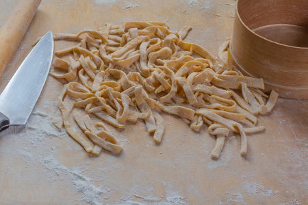 Heap of the raw freshly prepared homemade egg noodles in the shape of the long strips on a wooden board sprinkled with flourの写真素材