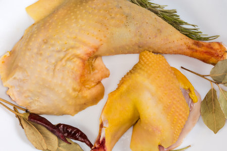 Raw leg and shoulder of rooster grown on the farm by free range method outdoors with yellow skin among the different dry spices on dish, top view of fragment close-upの写真素材