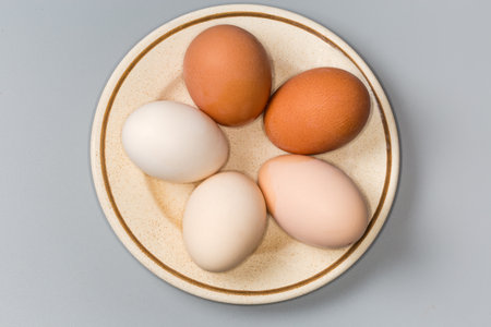 Whole boiled chicken eggs in the shells of different shades from white to brown on saucer on a gray background, top viewの写真素材