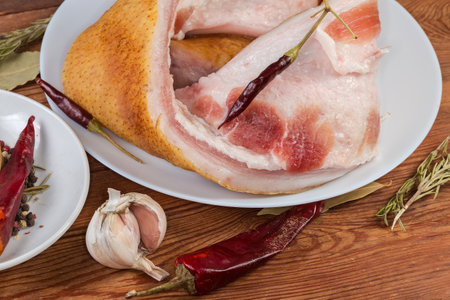 Pieces of the salted pork fatback on skin with meat layers on white dish among the different dry spices and fresh garlic, fragment close-upの写真素材