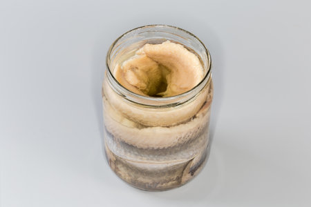 Pickled herring fillets without skin in cooking oil in open glass jar on a gray backgroundの写真素材