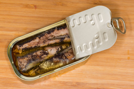 Canned sardines in cooking oil in small partly opened tin can with ring-pull tab lid on a wooden surface, top viewの写真素材
