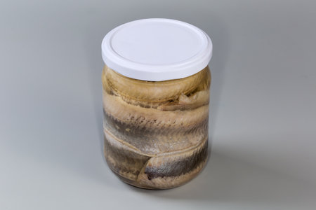 Pickled herring fillets without skin in cooking oil in sealed glass jar on a gray backgroundの写真素材
