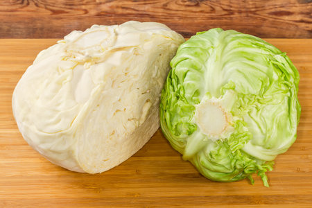 Whole head of the young fresh white cabbage and halved head of late white cabbage of last year's harvest on a wooden cutting boardの写真素材
