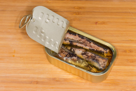 Canned sardines in cooking oil in small partly opened tin can with ring-pull tab lid on a wooden surfaceの写真素材