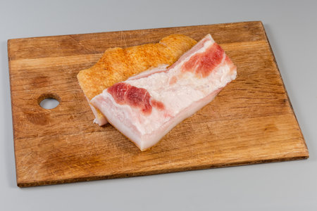 Long pieces of the salted pork fatback on skin with meat layers on cutting board on a gray backgroundの写真素材