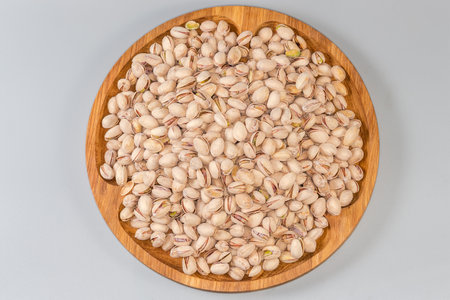 Heap of the roasted salted pistachio nuts with partly open shells on a big wooden dish on a gray background, top viewの写真素材