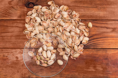 Partly peeled roasted salted pistachio nuts on the transparent glass saucer against the empty shells on a rustic table, top viewの写真素材