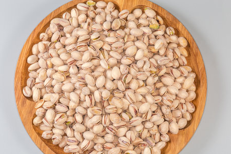 Heap of the roasted salted pistachio nuts with partly open shells on a big wooden dish on a gray...