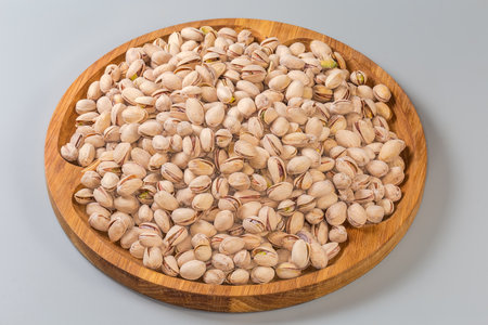 Heap of the roasted salted pistachio nuts with partly naturally open shells on a big wooden dish on a gray backgroundの写真素材