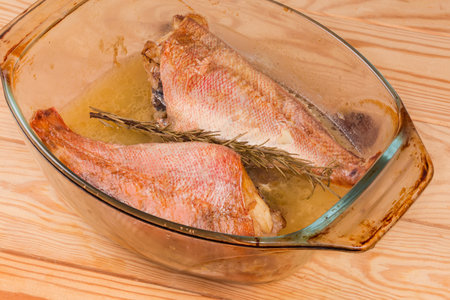 Two baked redfishes without heads, also known as ocean perch in the old glass baking dish on a rustic table, fragment close-upの写真素材