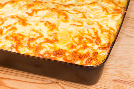 Partly browned melted cheese on top of the freshly baked vegetable casserole in baking tray, fragment close-up in selective focusの写真素材