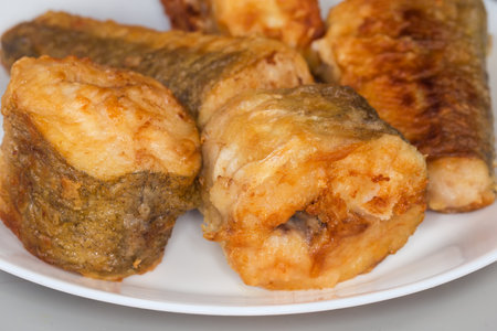 Fried pieces of hake hubbsi, or Argentine hake on white dish, fragment close-up in selective focus