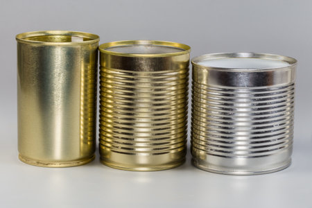 Different open empty tin cans from under a canned food, with various white and yellow covering on a gray background, side viewの写真素材
